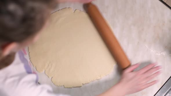 girl rolls dough on the table with a rolling pin alt