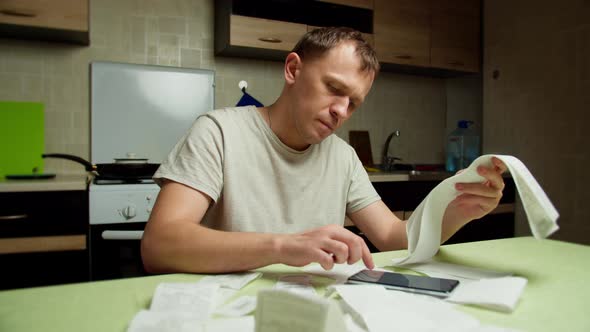 A Man Sitting in the Evening in the Kitchen Looks at Sales Receipts and Considers Family alt