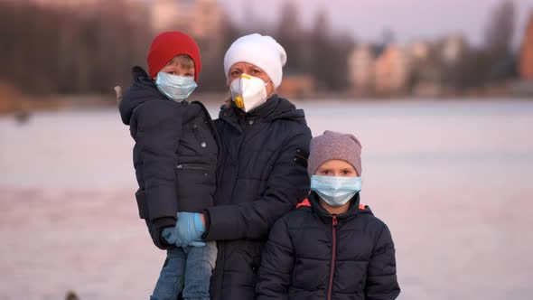 Mother, son and daughter in medical masks on the lake in the Park.