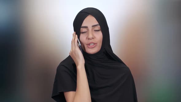 Portrait of a Beautiful Muslim Woman, a Female in a Hijab Communicates and Talks on a Mobile Phone alt