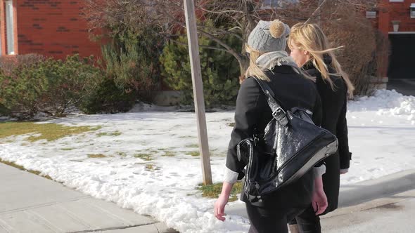 Two Young Females Walking Across The Street Talking In Winter From Behind