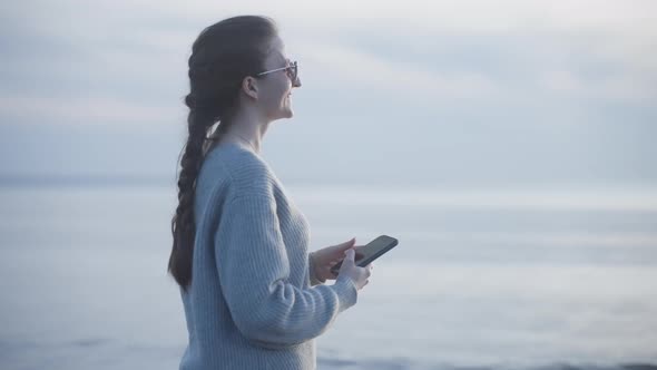 Young Beautiful Woman Points to Sea and Shoots Photo or Video on Smartphone