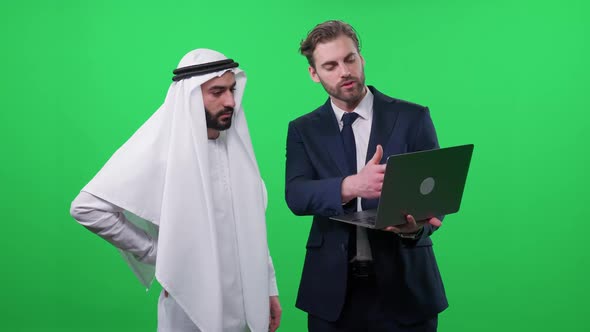 Businessman in a Suit Uses a Laptop and Communicate with a Arab Business Partner in a White Kandura alt