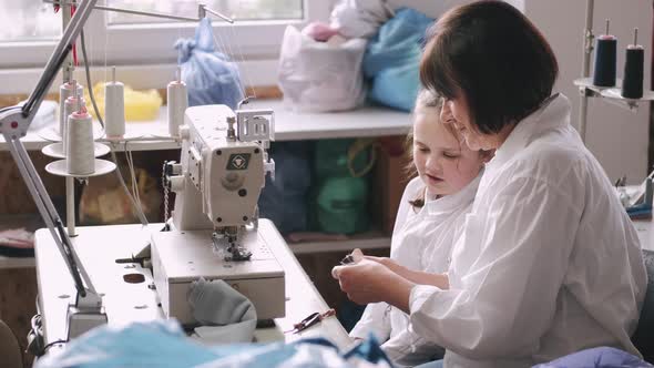 Grandma with Little Granddaughter Sew Clothes in the Factory alt