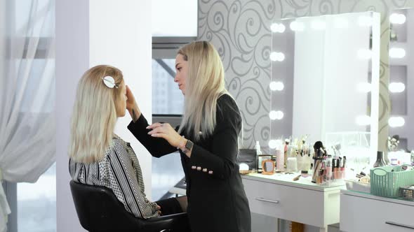Visagist Is Applying Foundation Cream on Woman's Face Using Brush in Salon
