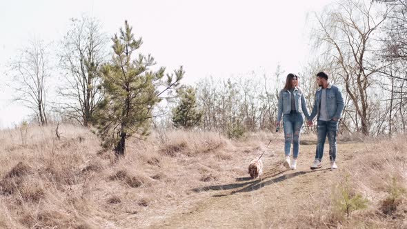 Young Man and Woman in Denim Are Walking in the Wheat Field with a Dog alt
