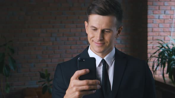 Male Professional Holding Smartphone Texting Message Standing in Office