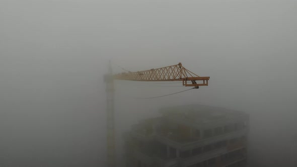 Birds eye view on tower crane boom in fog standing next to residential building. 