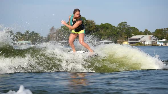 A young woman wake surfing behind a boat on a lake. alt