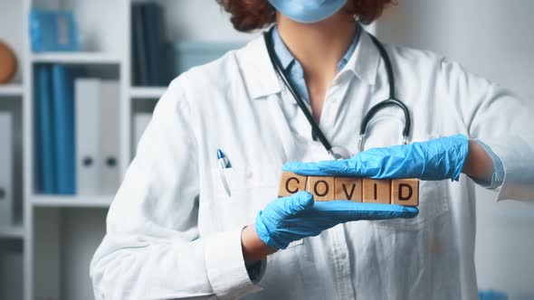 The Word Covid Is Held In Hands. A Doctor In A Medical Uniform Stands In A Hospital Medical Office alt