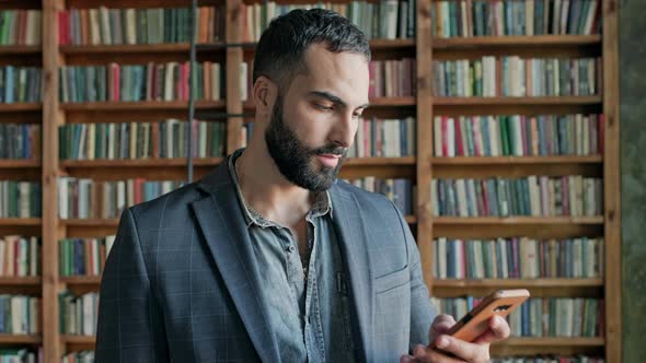 Young Man In The Library With Mobile Phone In His Hands alt