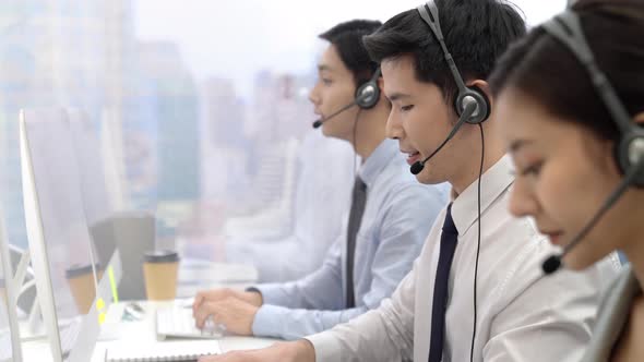 Handsome Asian man working in call center office as a customer service operator with team