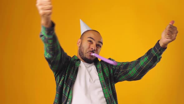 Happy African American Male in Party Cone Blowing Party Blower Against Yellow Background alt