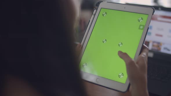 Close up hands young Asian woman using tablet with green screen on a table at home office.