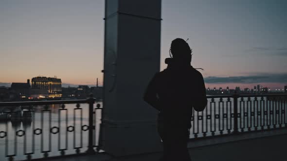 Silhouette of Active African American Guy Running on City Bridge in Evening Practicing Sport alt
