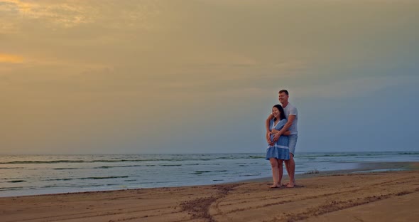 Beautiful Pregnant Woman Stands on the Shore with Her Husband and Laughs They are Happy
