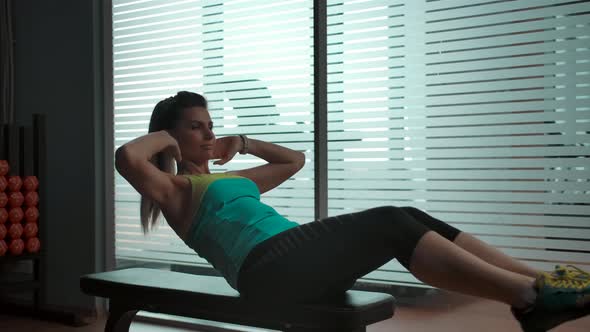 The Girl Does Abs Exercises on a Bench in the Gym Next to a Large Window alt