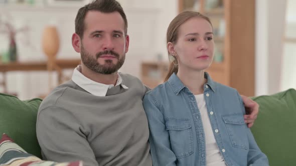 Happy Couple Smiling at the Camera While Sitting on Sofa alt