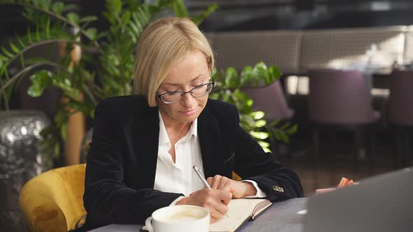 Portrait of Middle Aged Business Woman Writing in Notebook alt