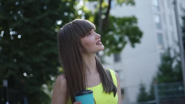 Pretty Girl with Glass of Beverage Admiring the Environment During a Walk alt