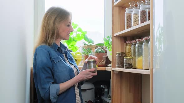 Storing Food in Pantry Mature Female Looking at Jar of Spices Holding Bowl of Green Apples