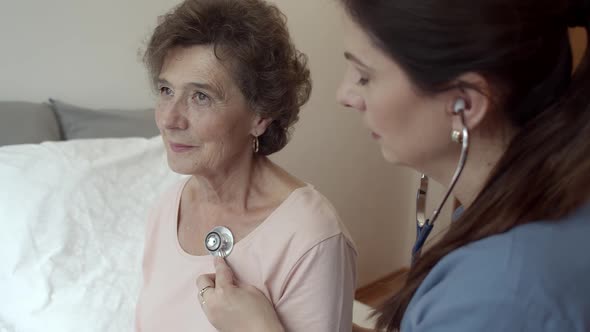 Home Nurse Listening For Breathing of Elderly Woman Sitting on Bed.