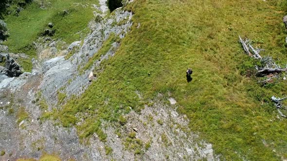 revealing aerial shot of a woman hiking on the edge of a mountain with a beautiful blue lake in the alt