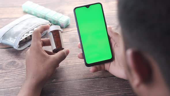 Rear View of Young Man Using Smart Phone and Holding Medical Pill Container alt