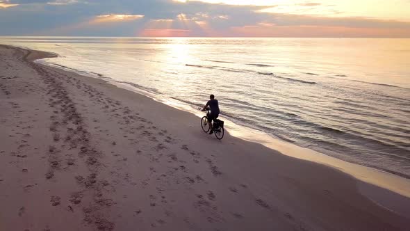 Man Riding Bicycle On Beach at Sunset.