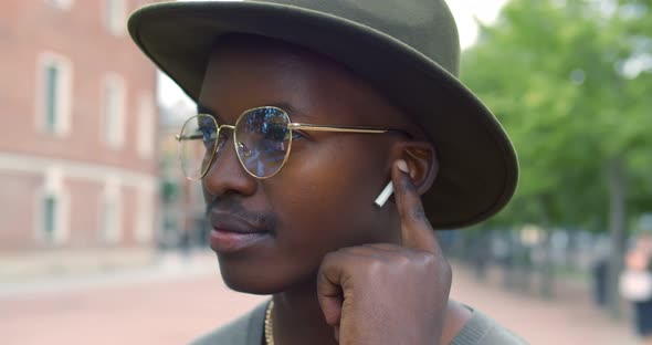 Close Up of Young Black Man Smiling While Using Earphones Outdoors alt