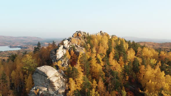 Aerial View of a Cliff Surrounded By a Colorful Autumn Forest at Sunset alt