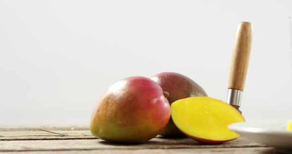 Halved and chopped mango with knife on wooden table alt