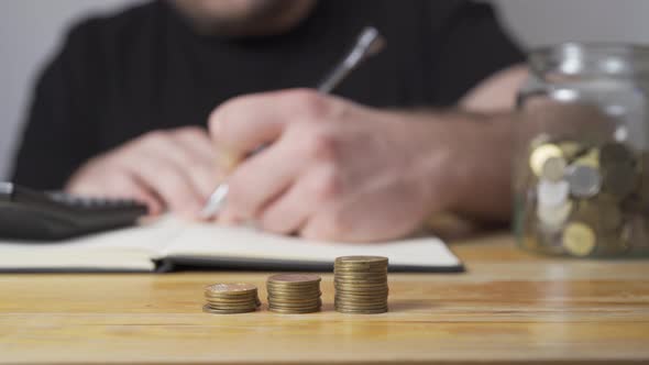 Stacks of Coins with Notepad, Calculator and a Jar in a Background