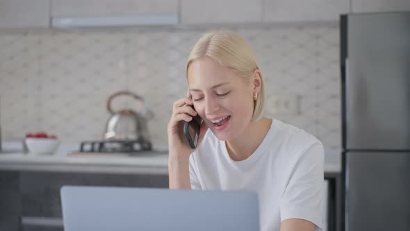 Cheerful Blonde Woman Says Bye on Phone Call When Sitting at Laptop in Kitchen