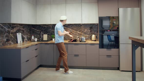 Man in a Hat Having Fun in the Kitchen While Cooking Dancing and Singing with a Ladle in His Hand