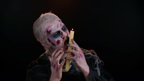 Sinister Man with Horrible Scary Halloween Zombie Makeup Making Faces Spells Conjures Over a Candle alt