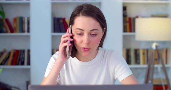 çSmiling Young Business Woman Talks on Smartphone Sitting at Home Office Desk Slow Motion alt