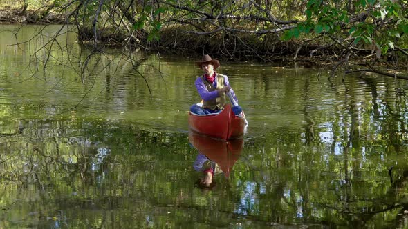 Cowboy in a Canoe Floats on the River in the Forest alt