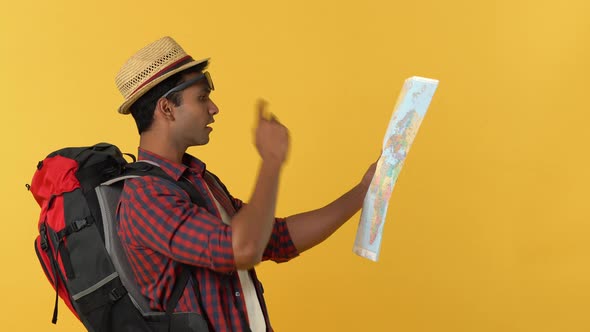 Smiling young Indian tourist man with his backpack finding location on the map