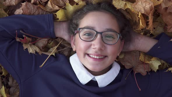 Happy School Girl Lies on Autumn Leaves and Smiling alt