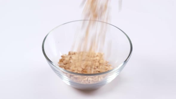 Oats or oat flakes falling in a glass bowl on white background.