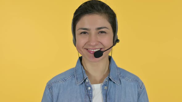Indian Woman with Headset Smiling at Camera, Yellow Background  alt