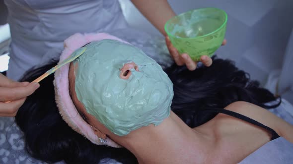 Cosmetologist Applies Alginate Mask with Spatula on Female Face