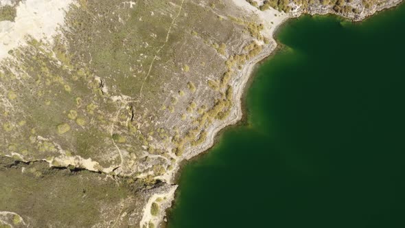 Bird eye perspective of a coastline with green colored ocean and a dry coutryside  alt