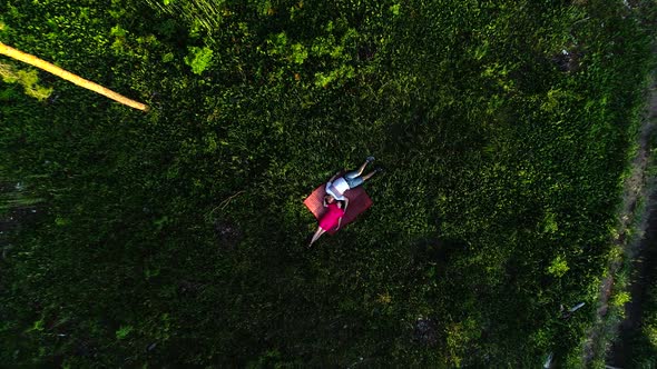 Top View of a Young Girl in a Pink Dress and a Guy Lie on a Blanket in a Green Grass. Aerial View.