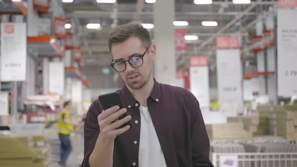 Young Man Shopping in Large House Furniture and Decor Store with Smartphone alt