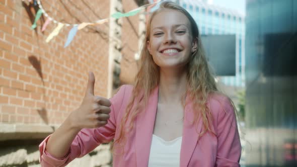 Slow Motion Portrait of Cheerful Young Woman Smiling and Showing Thumbsup Hand Gesture Outside alt