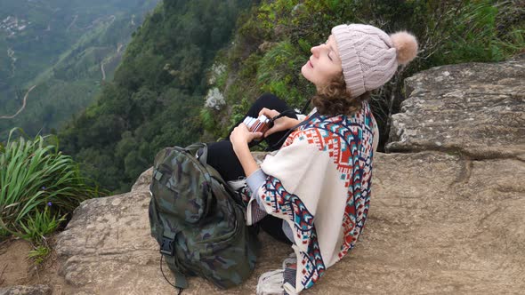 Young Woman With Backpack Sitting On A Cliff And Enjoying A View alt