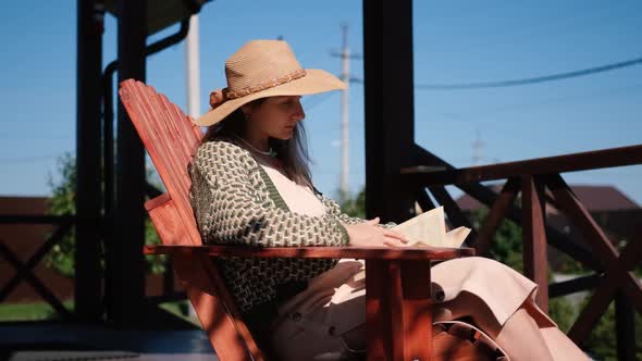 Young Woman Reading a Book on a Cozy Veranda at Home on a Summer Day Turning a Page alt