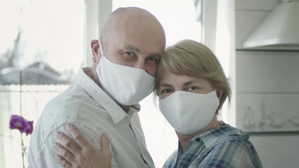 Portrait Of Mature Couple In Medical Masks In Guarantine. They Cuddle. alt